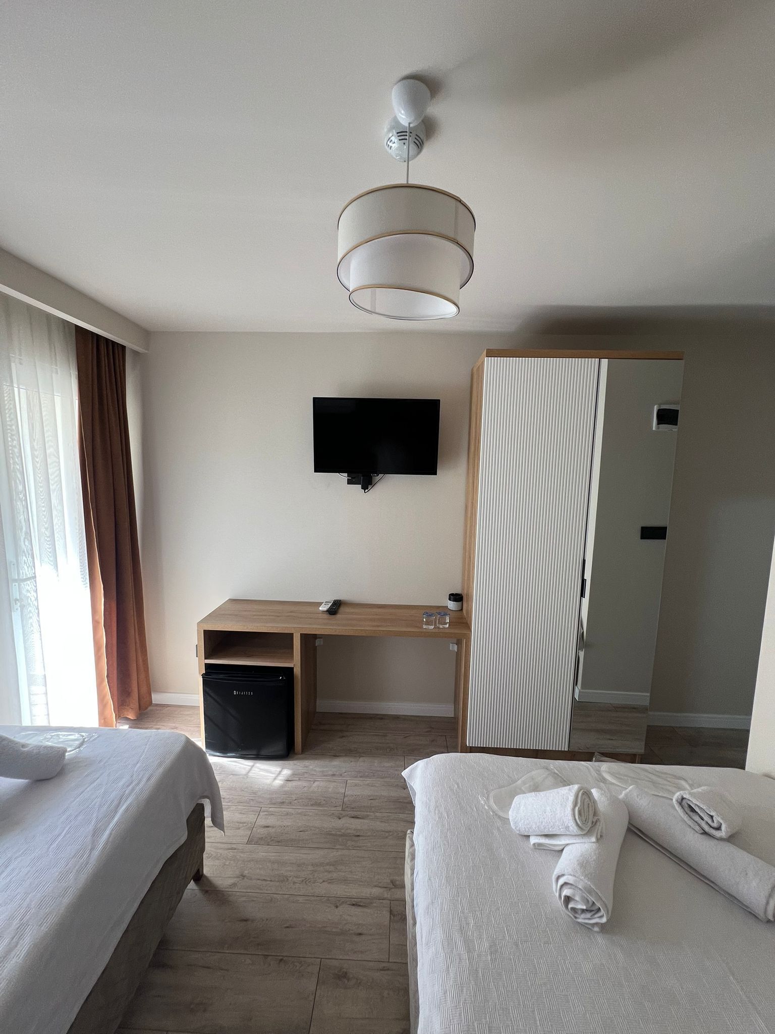 Quarto de hotel com duas camas, uma escrivaninha, uma televisão e um guarda-roupa.