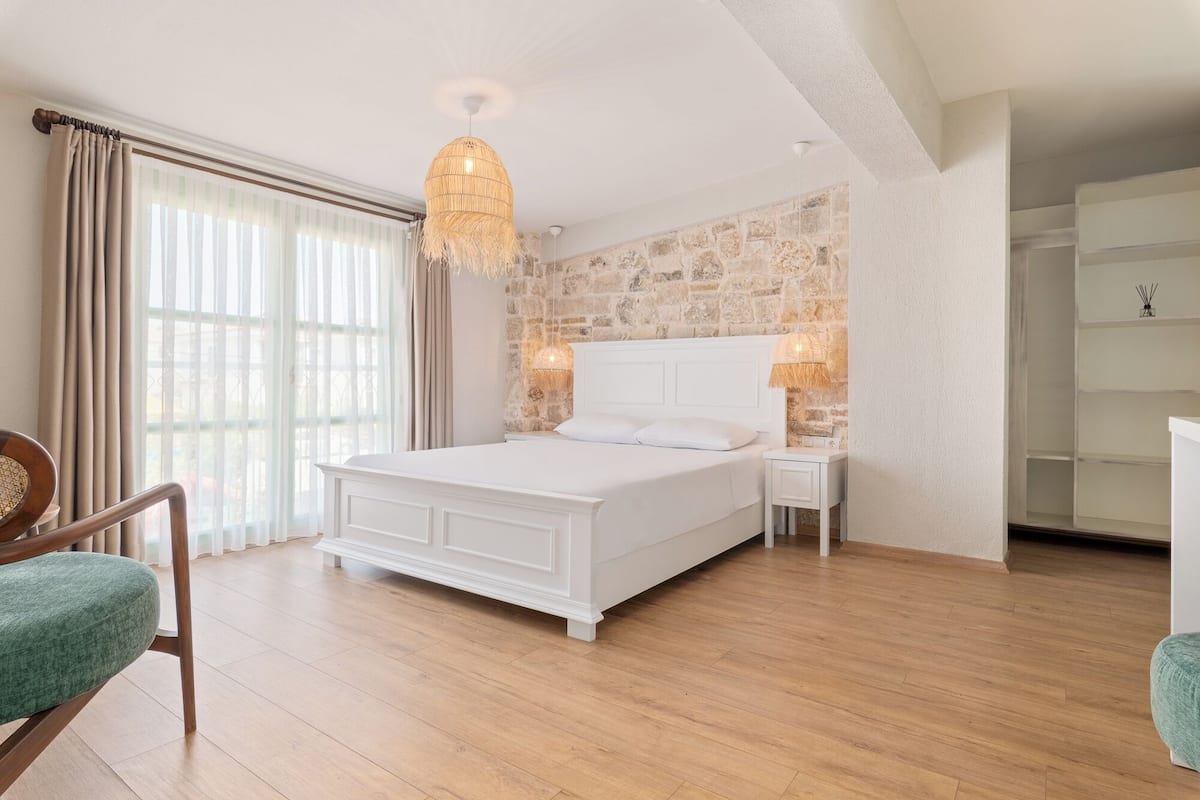 A bedroom with a large bed, wooden flooring, a stone wall, and a chandelier.