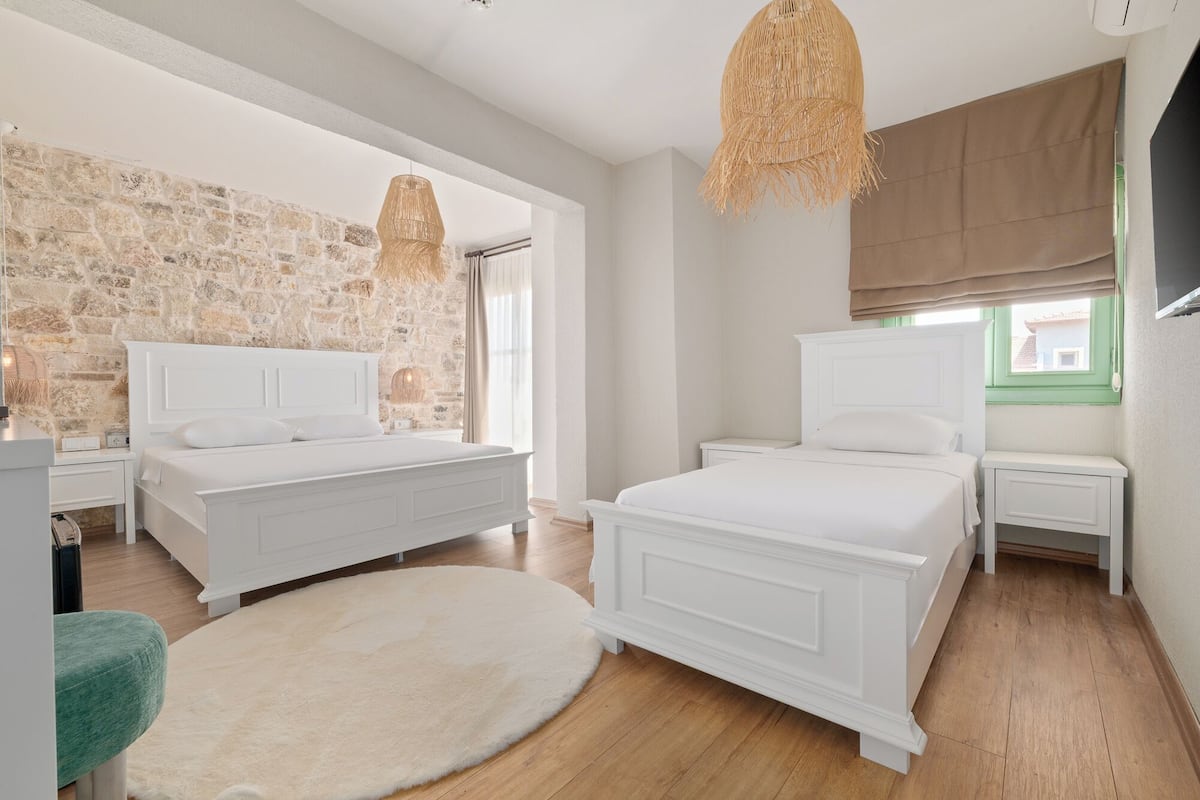 A bedroom with two white beds, a stone wall, a wooden floor, and a large window with a view.