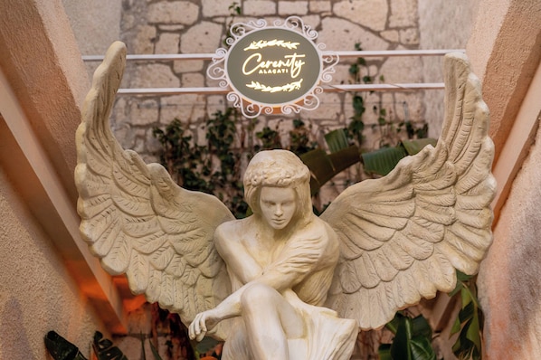 Estátua de um anjo com asas abertas, uma parede de pedra e uma placa com a inscrição 'Cerenity Alacati'.