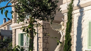 Ein Steingebäude mit einer Statue, grünen Fensterläden und einem weißen Zaun.