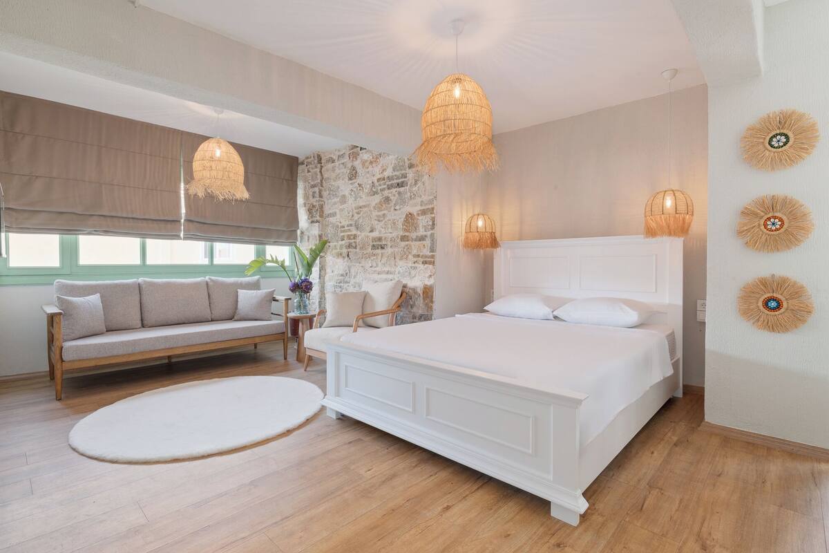 A bedroom with a large bed, a sofa, and a stone wall.