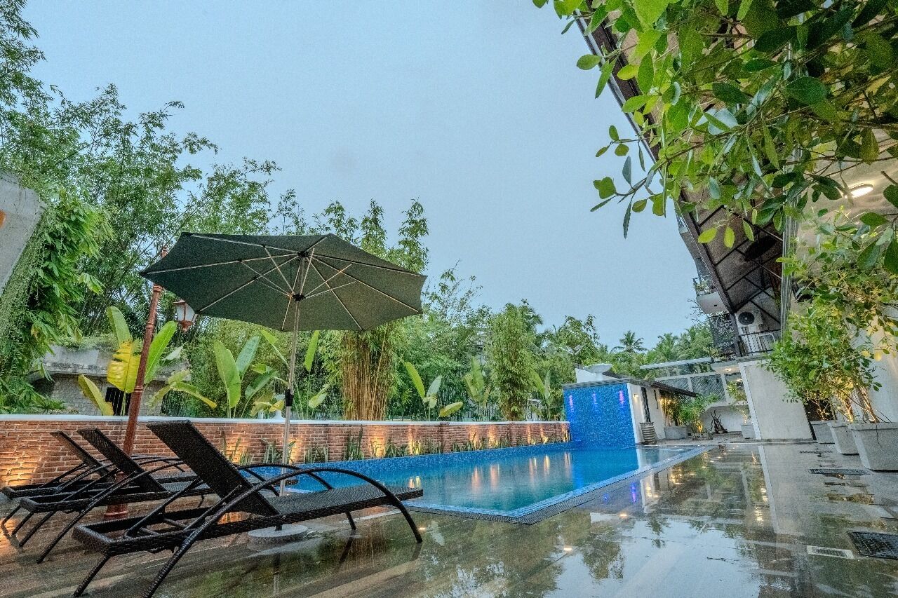 A swimming pool with lounge chairs and an umbrella, surrounded by lush greenery.