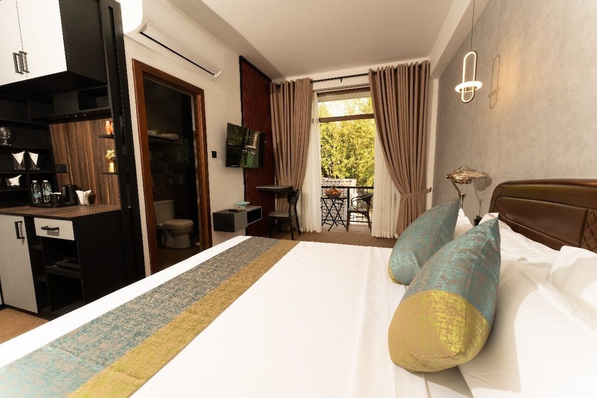 A hotel room with a bed, a desk, a chair, a small table, and a balcony with curtains.