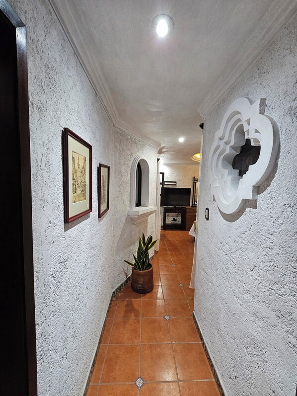 A hallway with white textured walls, framed pictures, a potted plant, and a decorative wall piece.