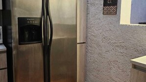 Ένα ψυγείο από ανοξείδωτο ατσάλι σε μια κουζίνα με πλακάκια στο δάπεδο και ένα διακοσμητικό πάνελ στον τοίχο.