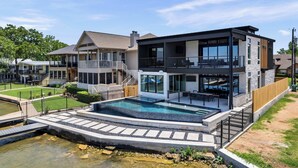 Ett modernt hus i två våningar med en swimmingpool, en täckt uteplats och utsikt över vattnet.