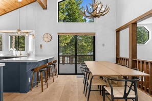 Una cocina moderna con una isla central, taburetes de bar, una mesa de comedor y una lámpara de araña grande.