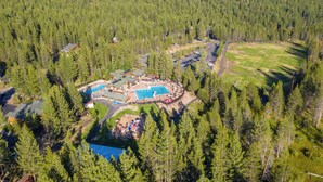 Vista aérea de un resort con piscina, cabañas para huéspedes y una zona boscosa.