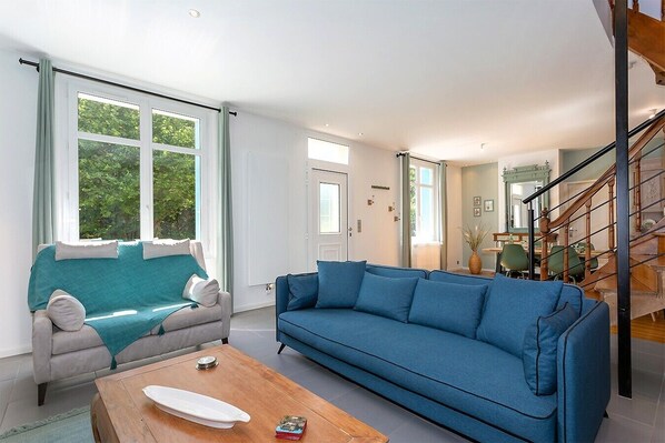 A modern living room with a blue sofa, a grey sofa with a teal throw, and a wooden coffee table.