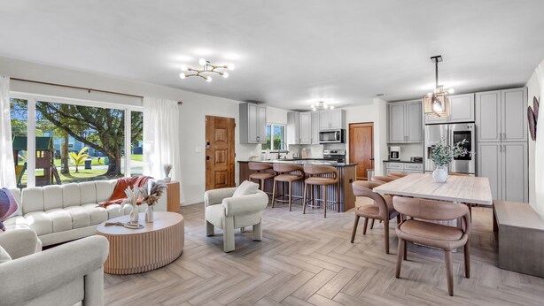 A modern kitchen with grey cabinets, a central island, and a dining area with a wooden table and chairs. - 4BR Biscayne River Home with Pool & Pickleball Fun (North Miami Beach)