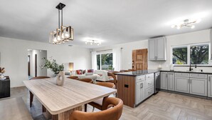 A modern kitchen with a central island, white cabinetry, and a dining area with a wooden table and leather chairs. - 4BR Biscayne River Home with Pool & Pickleball Fun (North Miami Beach)