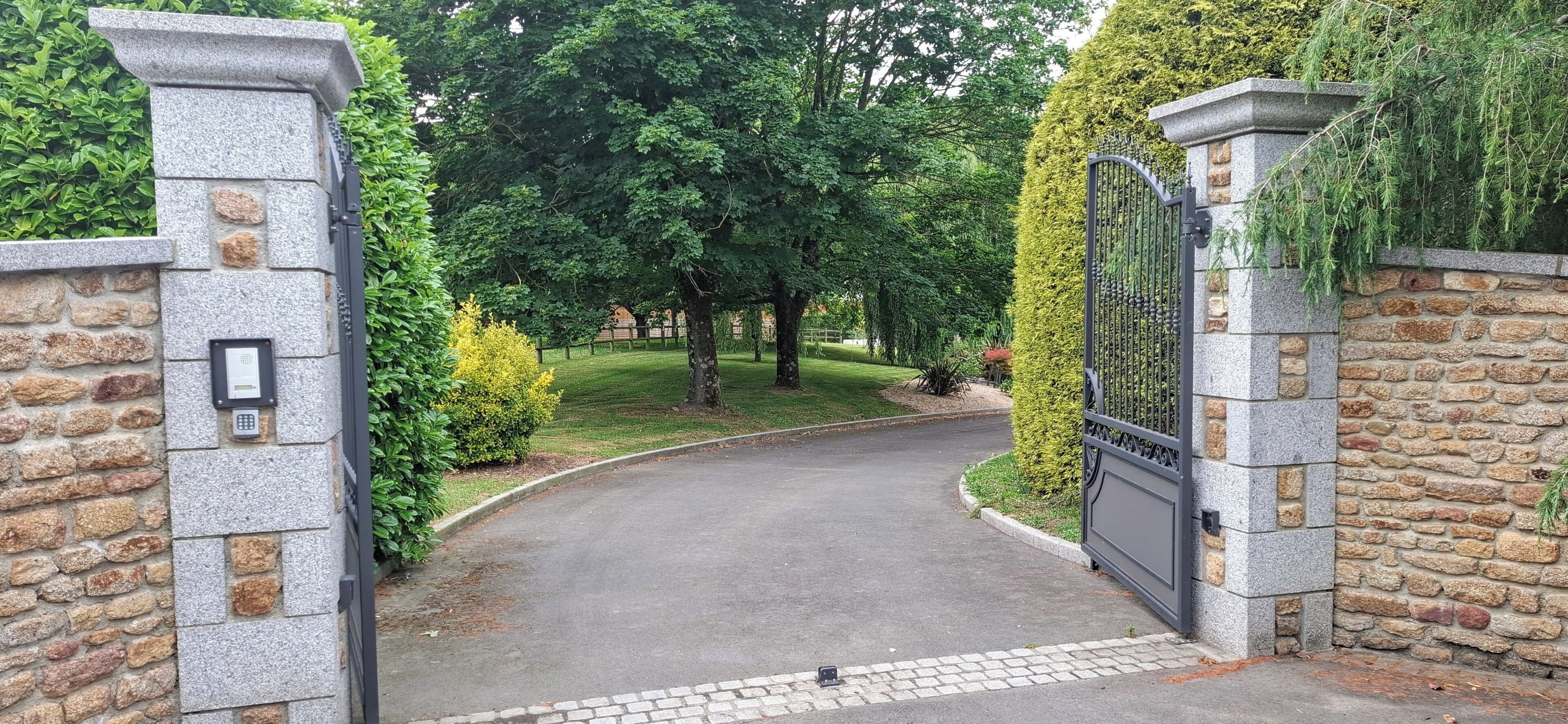 Un camino de entrada con puerta cerrada que conduce a un edificio con muros de piedra y una reja.