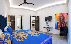 A modern bedroom with a large bed, a ceiling fan, a TV, and a painting on the wall.