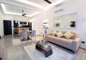 Un salon moderne avec une table basse en verre, un canapé beige et un coin repas comprenant des chaises et une table.