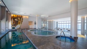 A modern indoor pool area with a large mural, glass-enclosed hot tub, and a view of the sky through large windows. - Tranquil 1 Bedroom Suite in Cabo San Lucas (Cabo San Lucas)