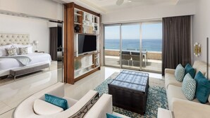 A modern hotel room with a bed, a TV, a sofa, and a view of the sea. - Tranquil 1 Bedroom Suite in Cabo San Lucas (Cabo San Lucas)