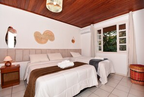 A bedroom with two beds, a wooden ceiling, a window with curtains, a bedside lamp, and wall decorations. - Apê a 150m da praia de Canasvieiras (Florianopolis)