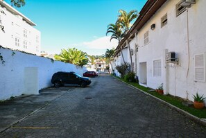 A narrow cobblestone street flanked by white buildings with small windows and air conditioning units. - Apê a 150m da praia de Canasvieiras (Florianopolis)