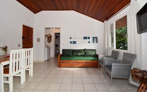 A living room with a wooden ceiling, a green sofa, a wicker chair, and a dining table with white chairs. - Apê a 150m da praia de Canasvieiras (Florianopolis)