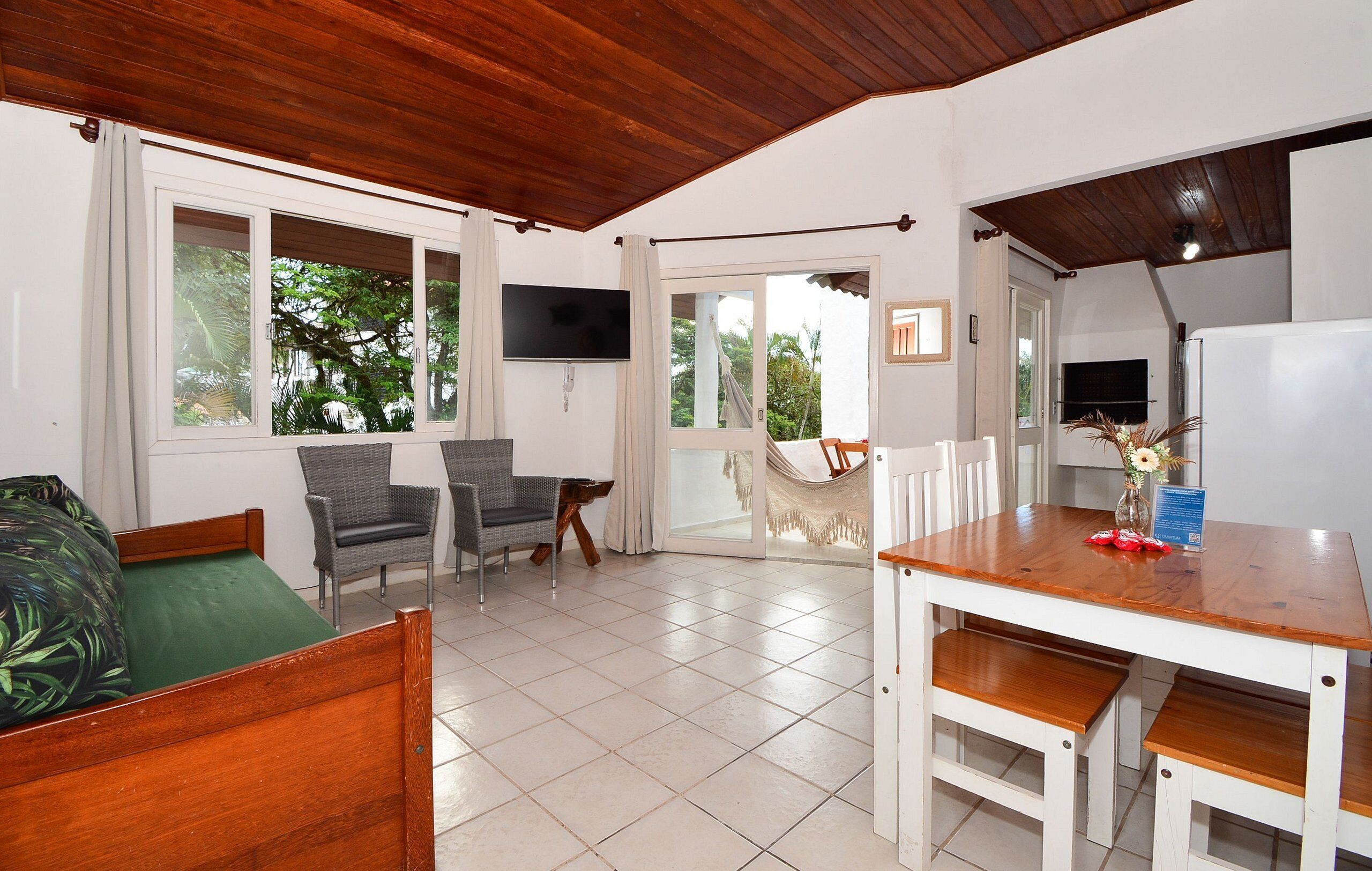 A room with a bed, two chairs, a dining table, and a TV mounted on the wall.