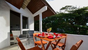 A wooden table with four chairs, a vase with flowers, and red napkins on a balcony with a view of trees.