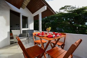 A wooden table with four chairs, a vase with flowers, and red napkins on a balcony with a view of trees. - Apê a 150m da praia de Canasvieiras (Florianopolis)