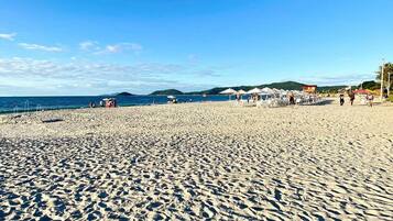 A wide sandy beach with umbrellas and beach chairs, a clear blue sky, and distant hills.