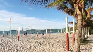 A beach volleyball court with palm trees and a clear sky.