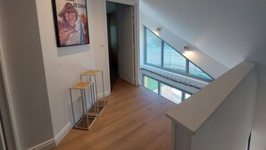 Un intérieur moderne avec un plancher en bois, un escalier menant à un balcon et une affiche accrochée au mur.