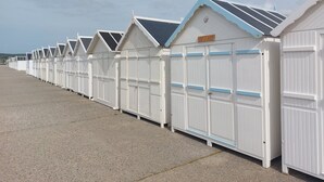 Une rangée de cabanes de plage blanches, avec des bordures bleues et une enseigne au-dessus de la porte.