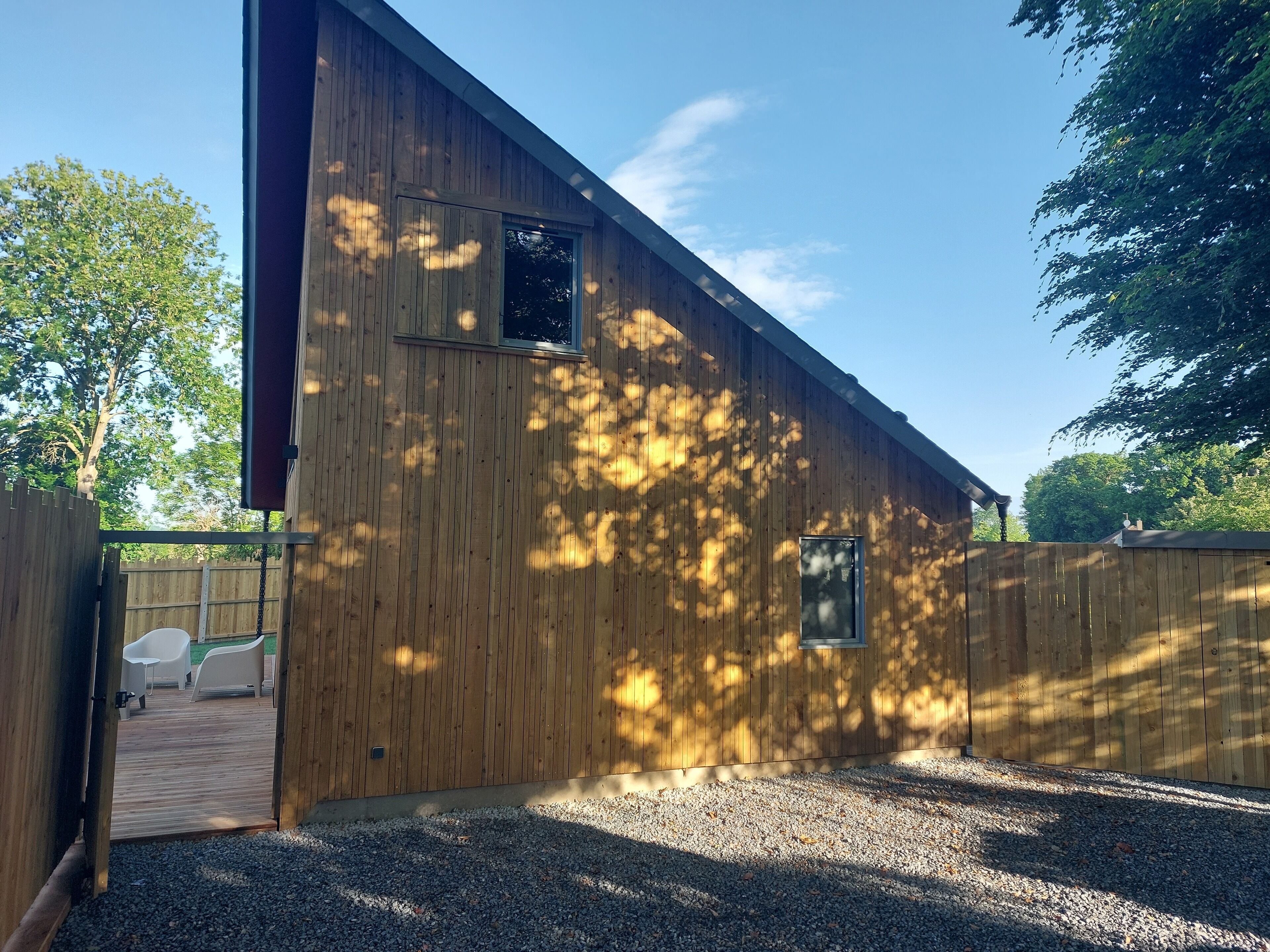 A wooden building with a gravel driveway and a wooden deck with two white chairs.