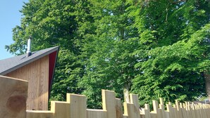 Une clôture en bois, avec un bâtiment rouge derrière.