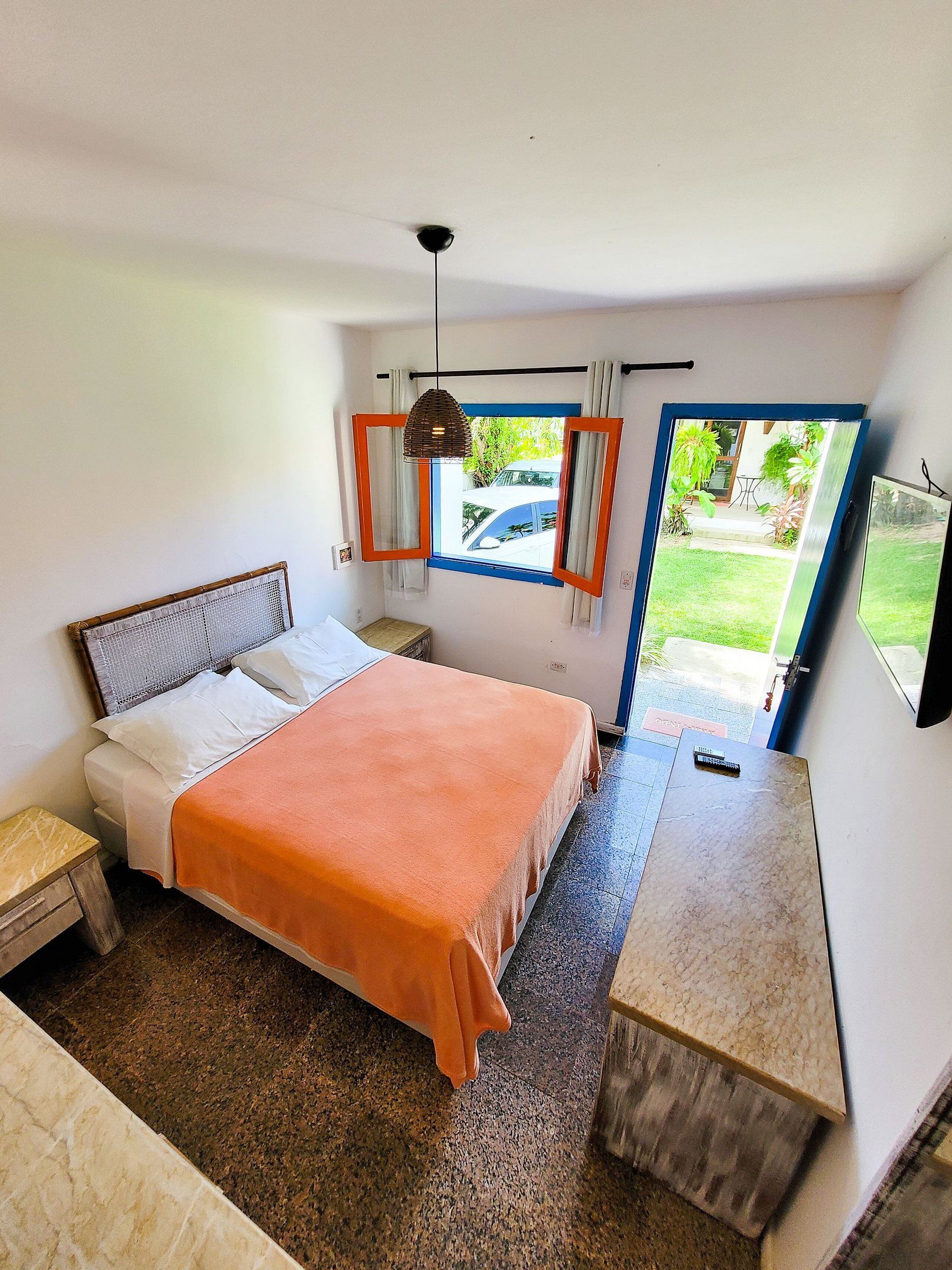 Une chambre à coucher comprenant un lit, une table de chevet, un bureau, un ventilateur de plafond et une fenêtre avec des rideaux.