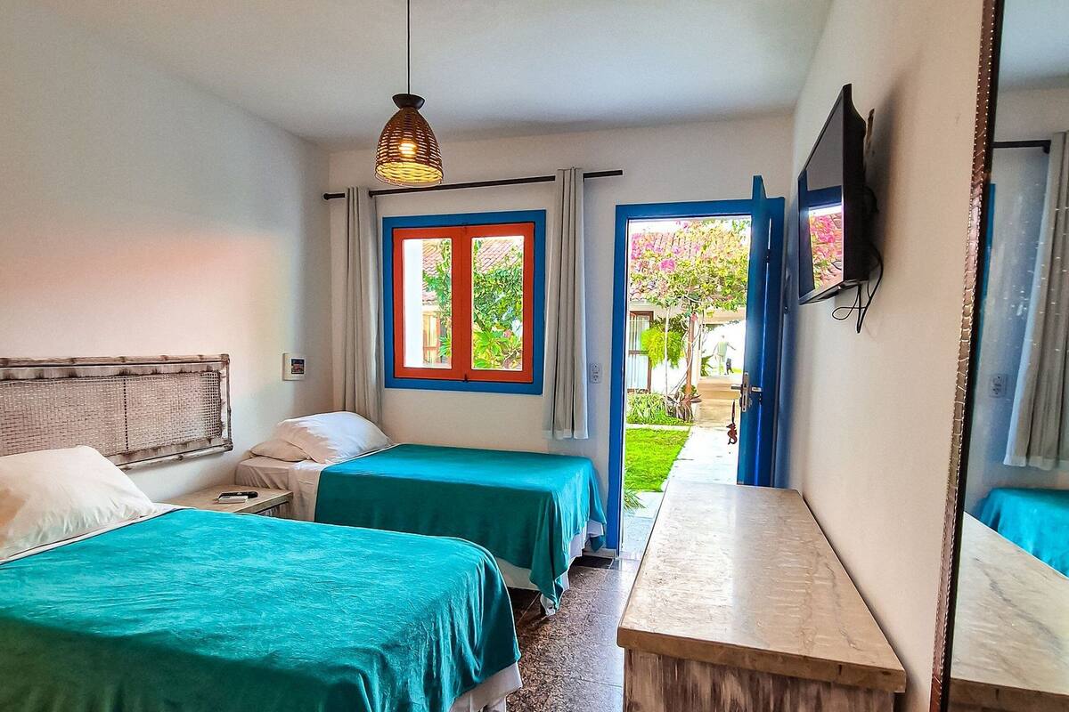 A hotel room with two beds, a desk, a television, and a view of the outside.
