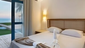 Quarto de hotel com uma cama, mesa de cabeceira, abajur e vista para o oceano através de uma porta de vidro.