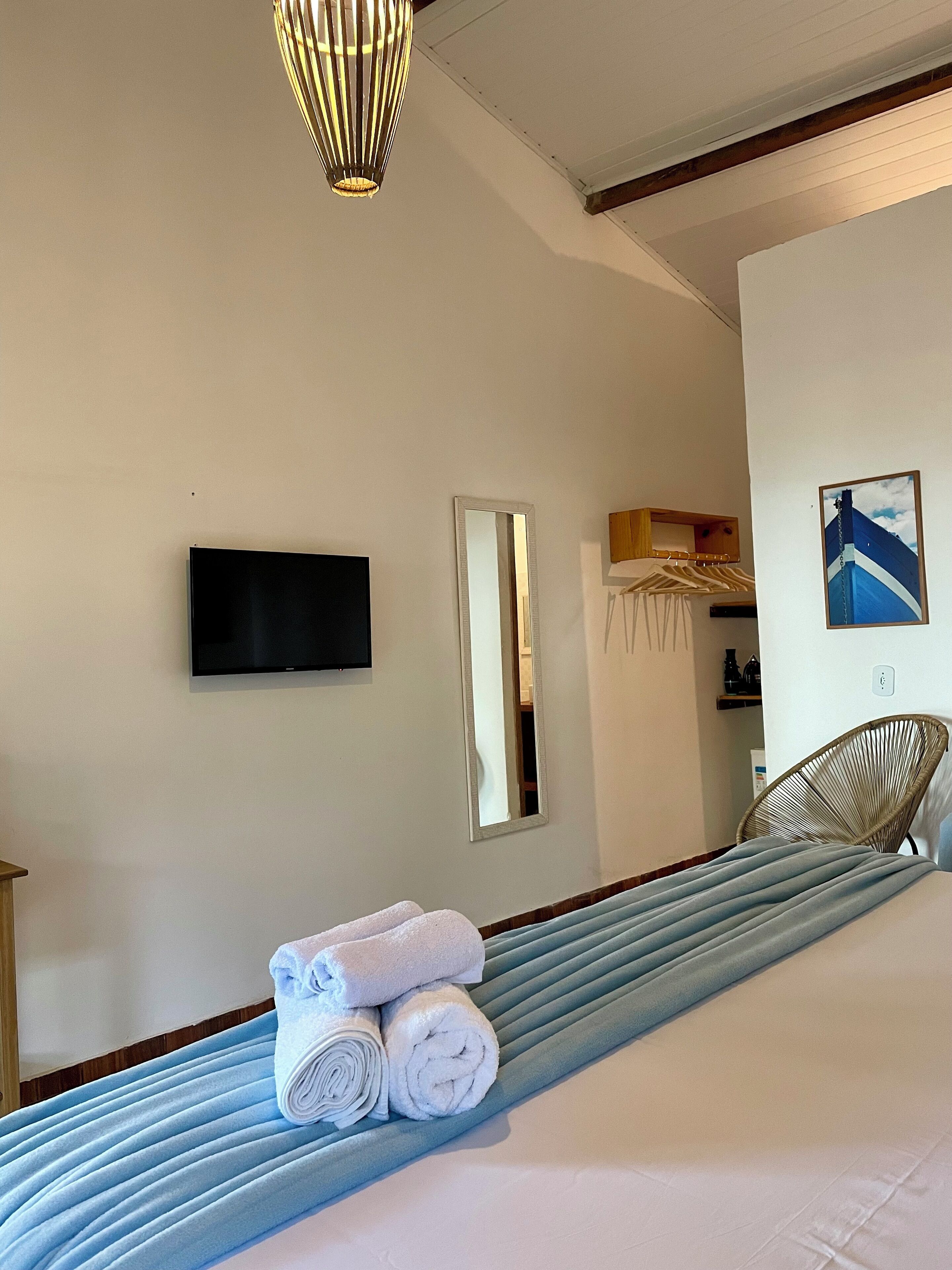 A hotel room with a bed, a flat-screen TV mounted on the wall, a mirror, and a picture of a ship.