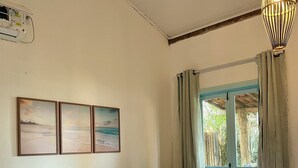 A neatly made bed with a blue blanket, a window with curtains, and three landscape paintings on the wall. - Pousada Safyra  (Porto Seguro)
