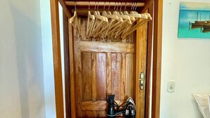 A wooden cabinet with a hanging rack, a power outlet, and a teal nightstand. - Pousada Safyra  (Porto Seguro)