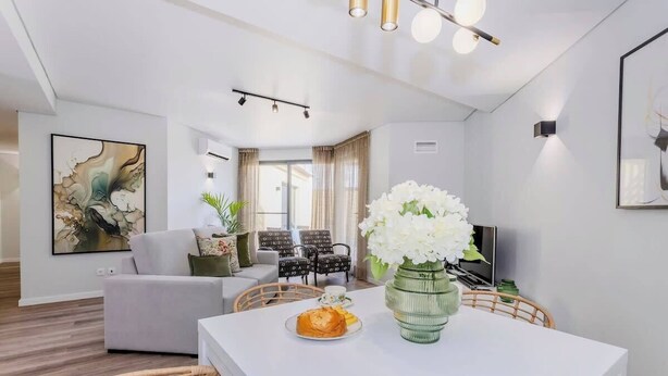 A modern living room with a white sofa, a dining table with a vase of white flowers, and a television. - Casa do Senhor do Colégio (Ponta Delgada)