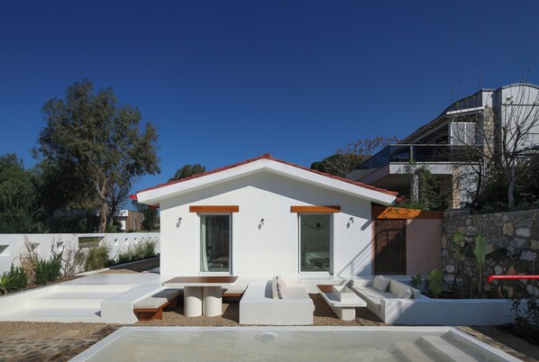 A modern house with a white exterior, red roof, and a patio area with seating.