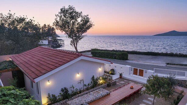 A coastal property with a red-roofed building, outdoor seating, and a view of the sea at sunset.