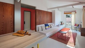 A modern living room with a wooden accent wall, a white sofa with colorful cushions, a red bench, and a red rug.