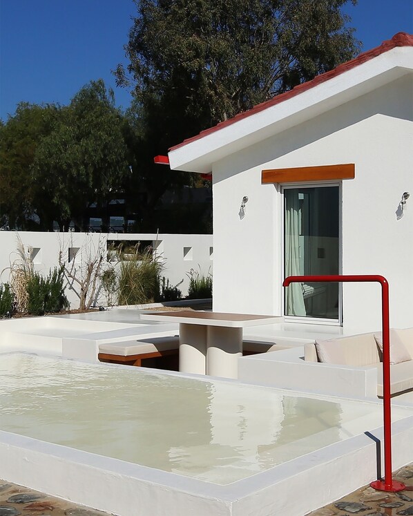 A modern outdoor pool area with a minimalist design, a red safety railing, and a white building with a glass door.