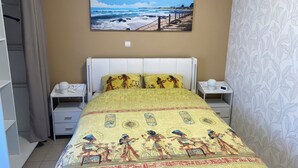 Un dormitorio con una cama y ropa de cama con motivos egipcios, una mesita de noche con una lámpara, una mesita junto a la cama con un teléfono y un cuadro de una playa en la pared.