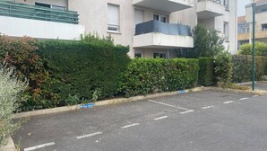 Un edificio residencial de varios pisos con balcones, una zona de estacionamiento y un seto.