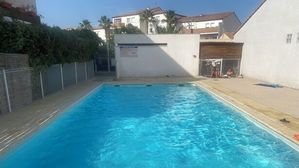 Una piscina rectangular con agua azul cristalina, rodeada por un bordeado de baldosas y una valla metálica.