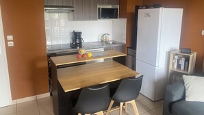 Una cocina compacta con una mesa de madera, dos sillas negras, un refrigerador blanco y un microondas sobre la estufa.