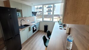 A modern kitchen with a black refrigerator, a microwave, and a sink. There is a window providing a view of buildings outside. - Hyper center, 3 bedrooms, 3 bathrooms, Free parking, Beach 20 minutes away! (Saint-Nazaire)