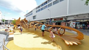 A playground with wooden structures and benches, a sidewalk, and storefronts in the background. - Hyper center, 3 bedrooms, 3 bathrooms, Free parking, Beach 20 minutes away! (Saint-Nazaire)